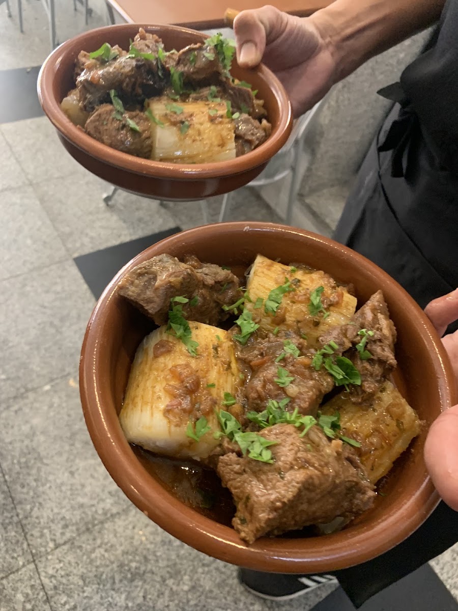 Duas tigelas de barro seguras nas mãos, com guisado de carne de vaca, batata e salsa fresca