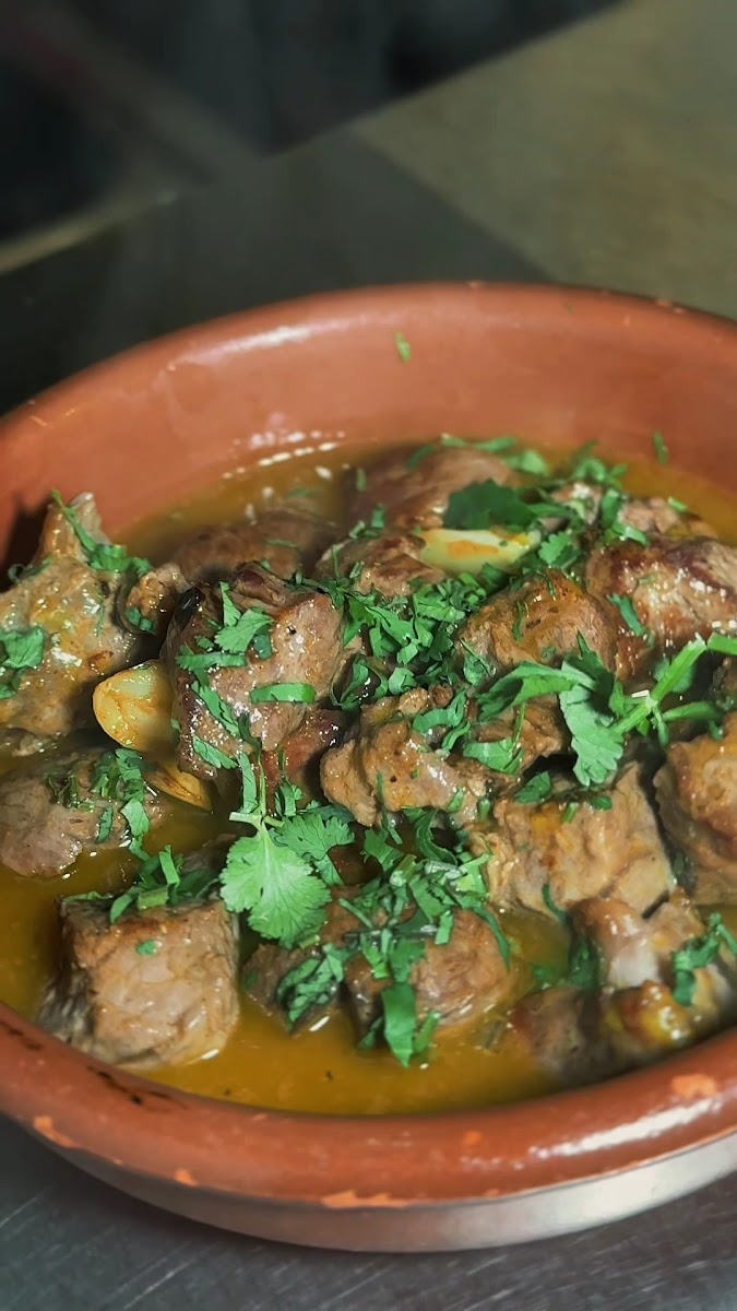 Tigela de barro com guisado de carne e cebolinhas num molho dourado, com salsa fresca por cima
