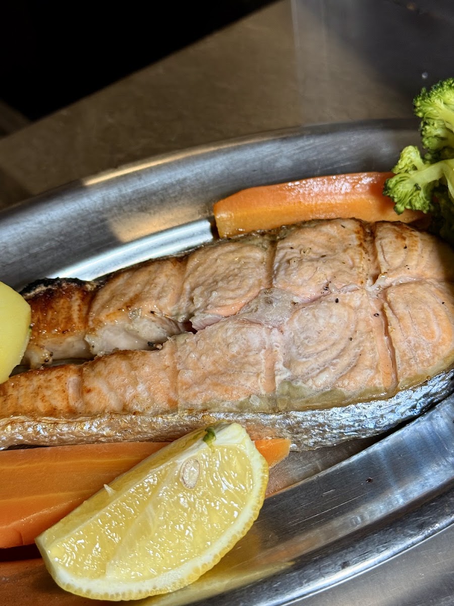 Salmão grelhado numa travessa de metal com cenoura, brócolos e batata cozidos ao vapor e uma fatia de limão