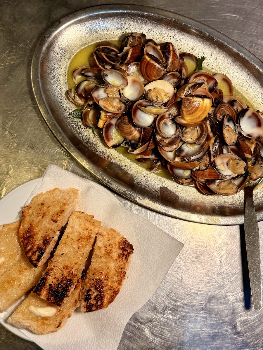 Travessa de prata com amêijoas em molho de alho e pão fatiado ao lado